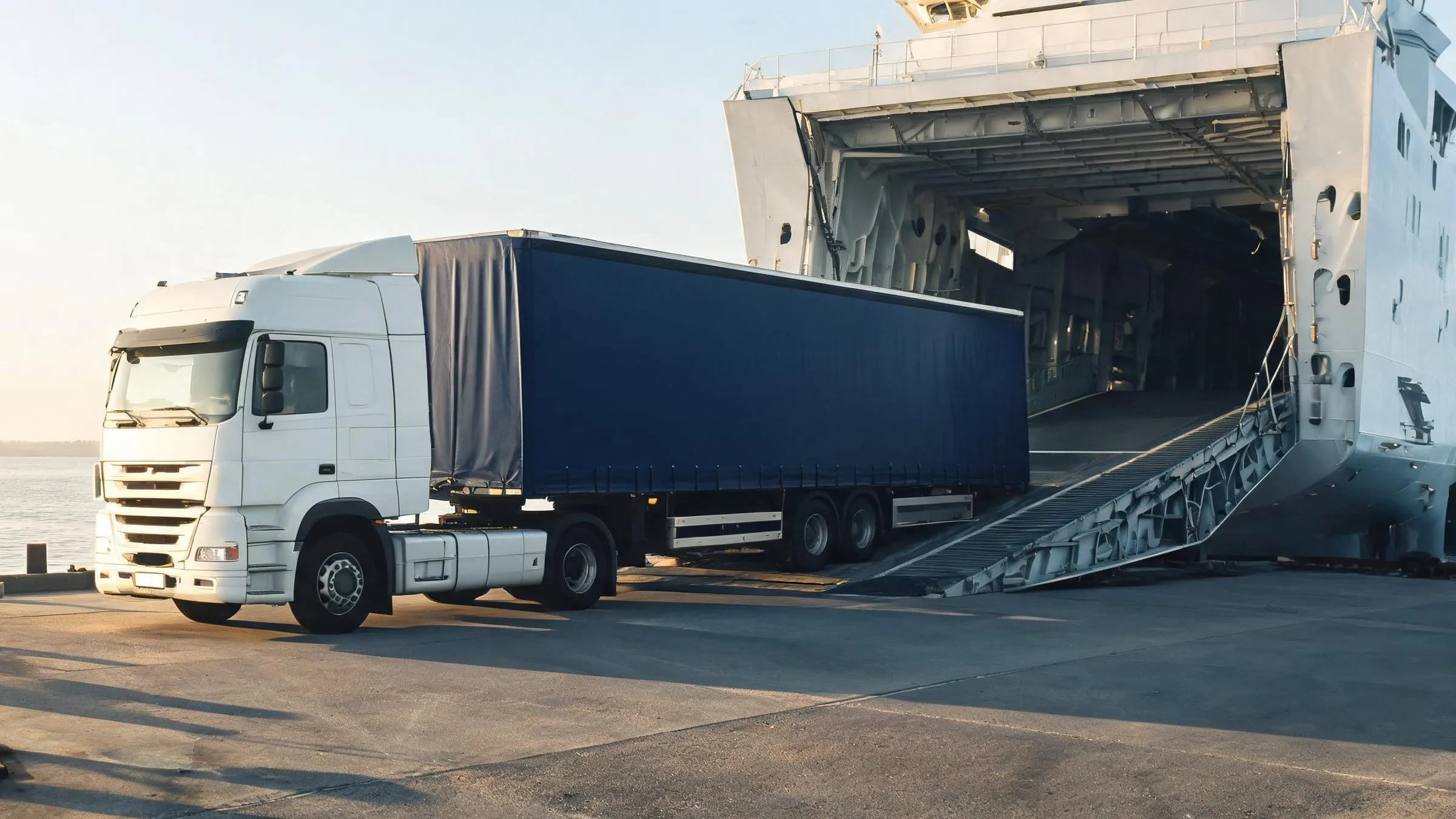 A truck with a curtainsider trailer driving onto a ferry in a port