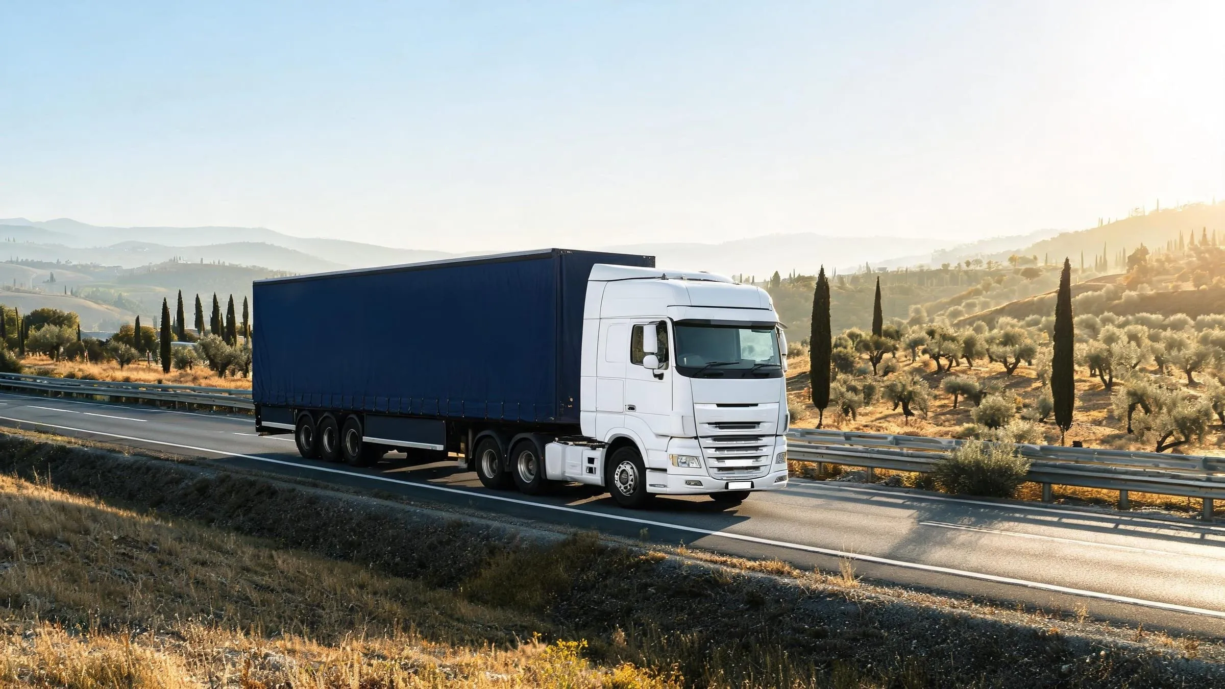 Camion avec semi-remorque tautliner sur une autoroute entre des collines sèches plantées d’oliviers et de cyprès